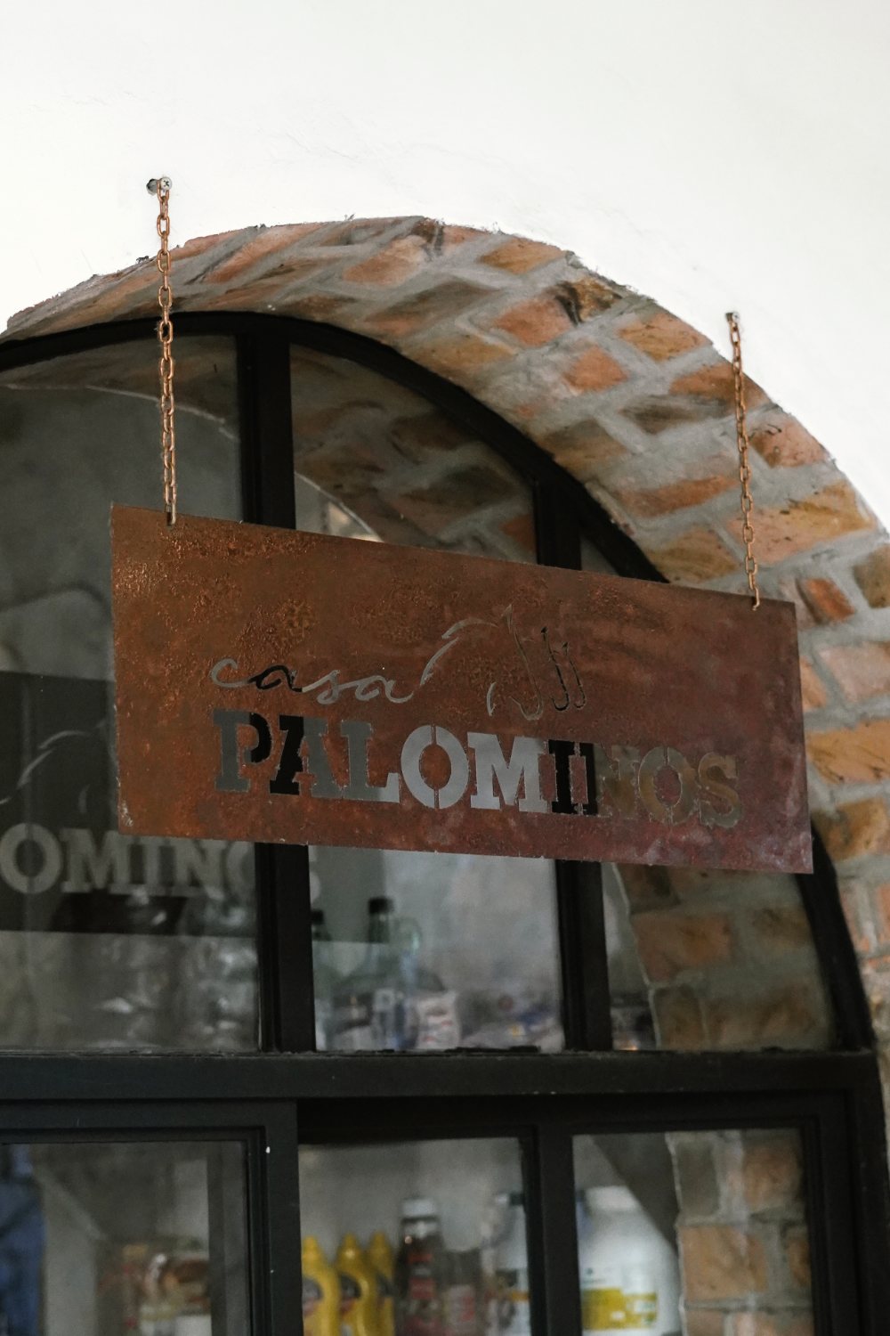 Letrero de acero oxidado de Casa Palominos colgado bajo el arco de ladrillo de la cocina.