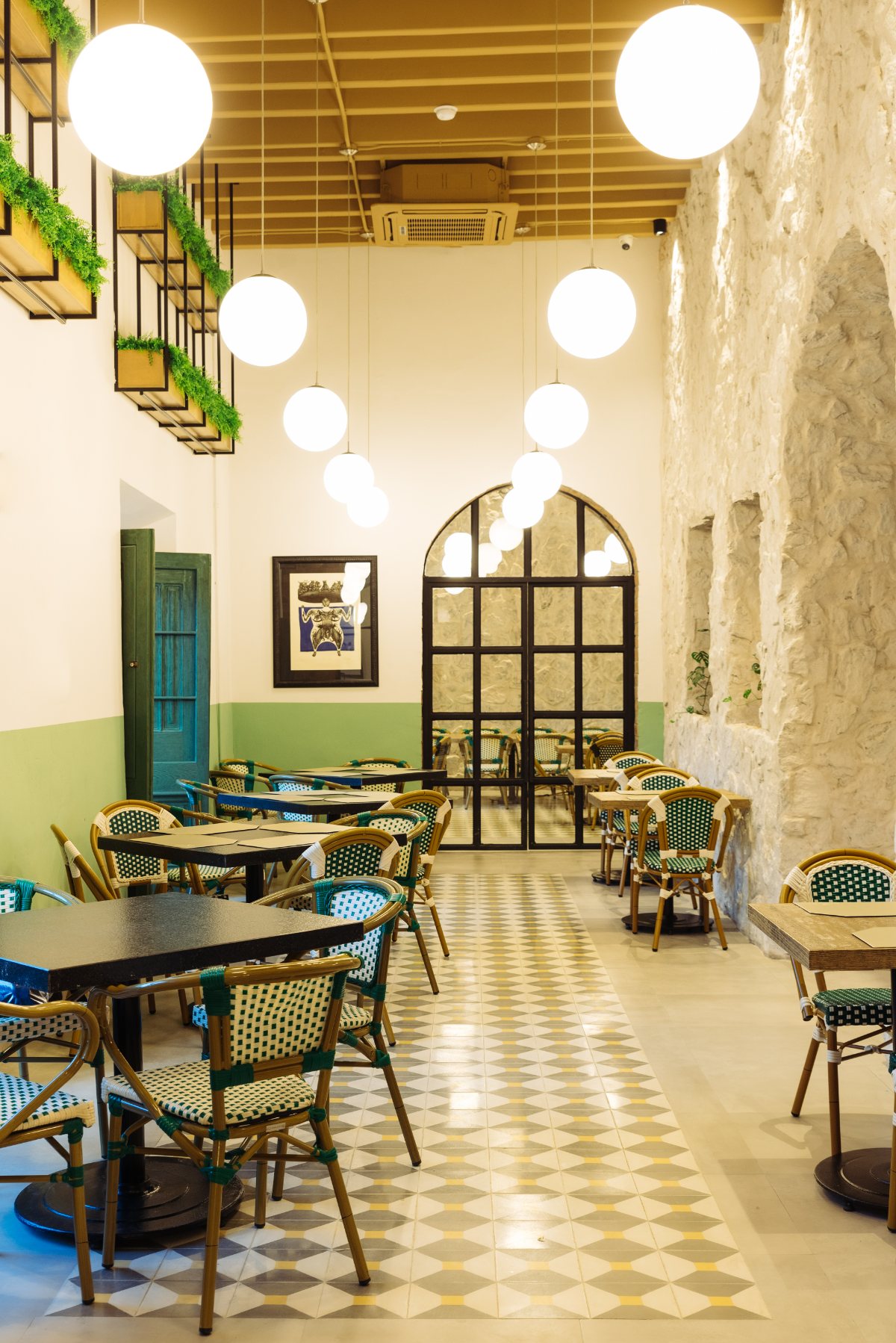 Pasillo de la casona con mesas de bistró, zoclo verde salvia y piso de pasta bajo techo de vigas.