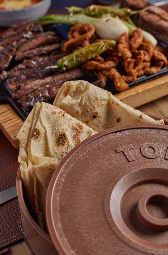 Arrachera, chorizo, cebollitas y chiles toreados en plancha, con tortillas recién hechas en el tortillero.