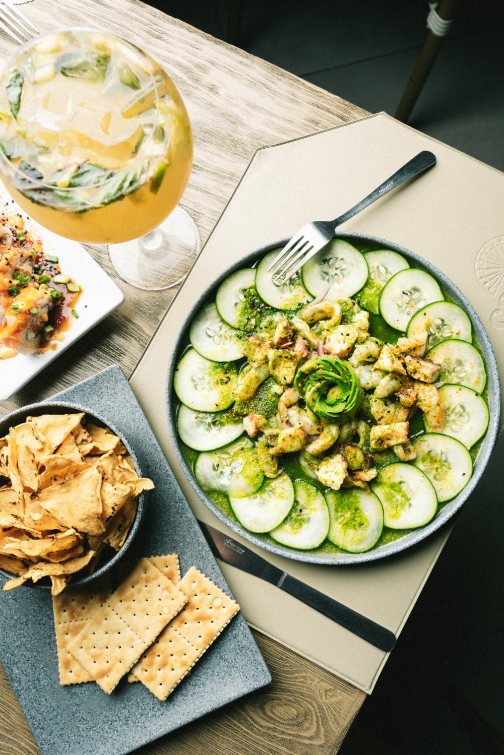 Mariscos sobre rodajas de pepino con salsa verde y rosa de aguacate, servidos con totopos y galletas saladas.